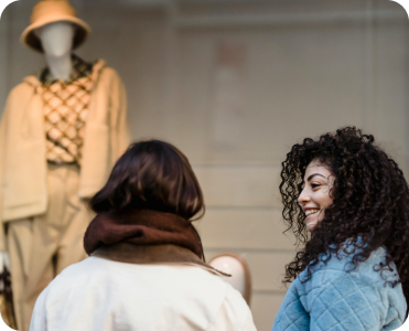 Duas mulheres observando a vitrine de uma loja de moda, destacando o interesse do público em campanhas locais.